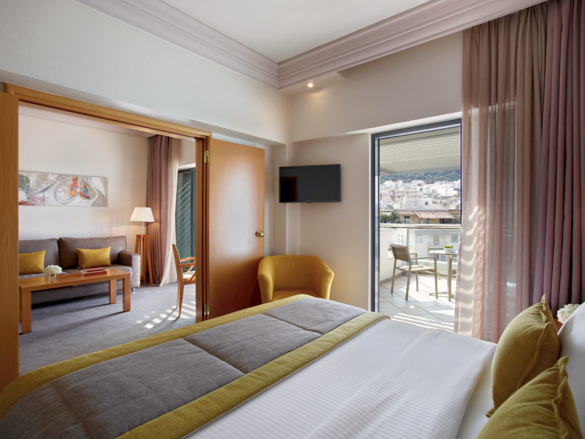 A modern hotel bedroom with a flat-screen TV, a bed, and curtains opening to a balcony with a city view.