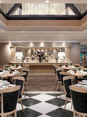 A stylish dining room set for an elegant meal, with neatly arranged tables, candles, flowers, and modern ceiling lights.
