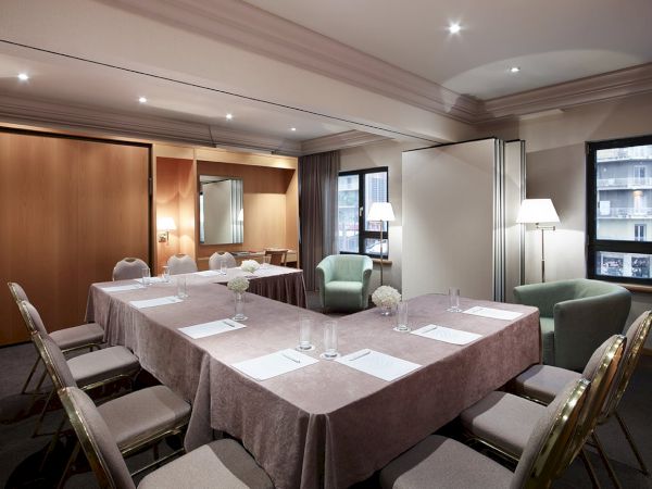 A modern conference room with a long covered table, place settings, cushioned chairs, and windows with city views.