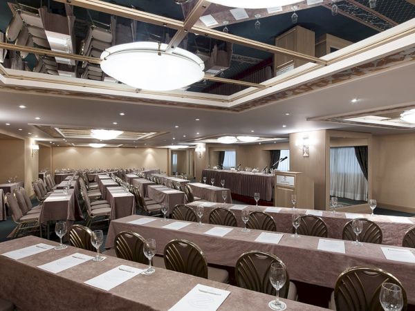 A formal banquet hall with long set tables, chairs, place cards, and a podium, prepared for an event.