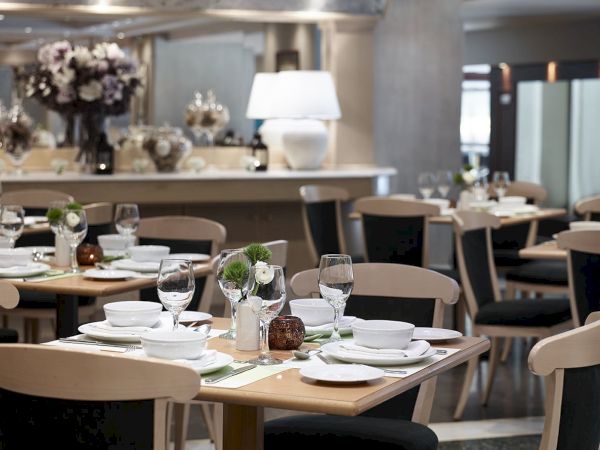 A neatly set upscale restaurant table with wine glasses, white plates, small floral centerpieces, and neatly arranged chairs.