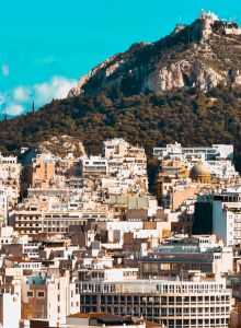 A sprawling city below a rocky hill crowned with a small white mosque and towers under a bright blue sky.