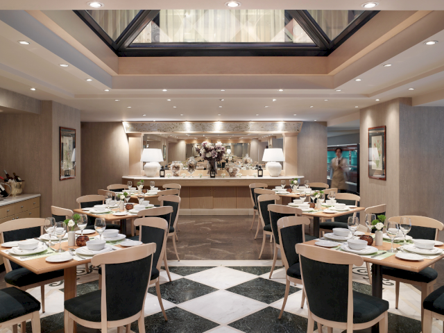 Upscale dining room with set tables, glassware, and flower centerpiece under warm lights.