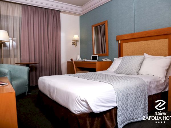 A neatly made hotel room with a double bed, bedside tables, lamps, a desk with laptop, and burgundy curtains.
