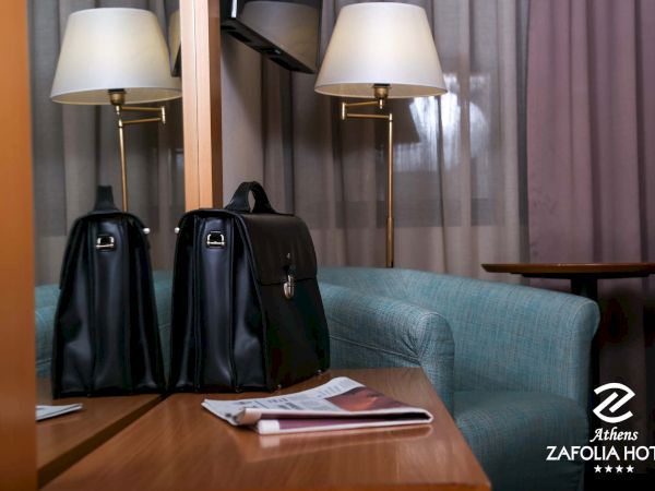 A hotel room scene with two black suitcases on a blue bed, flanked by bedside lamps and curtains.