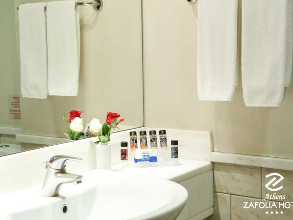 A hotel bathroom sink with rolled white towels, red-and-white roses, and toiletries on a counter.