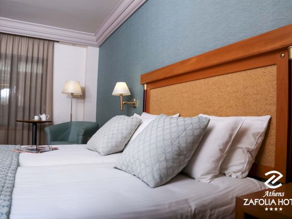 A hotel room with a neatly made bed, pillows, bedside lamps, curtains, and blue patterned walls.