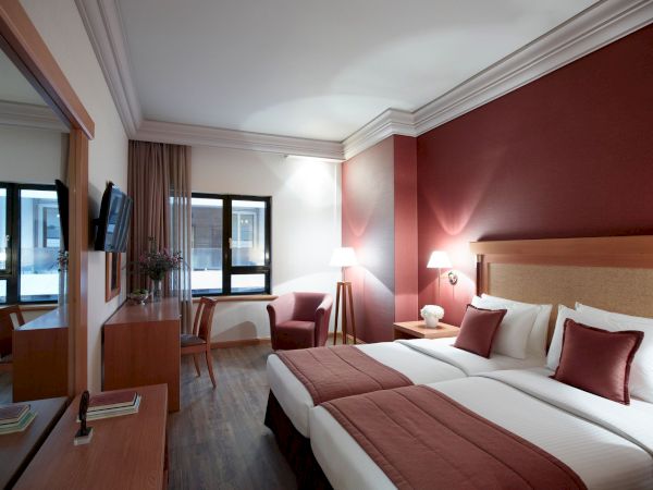 A modern hotel room with a neatly made bed, bedside lamps with warm lights, and a seating area by large windows and curtains.