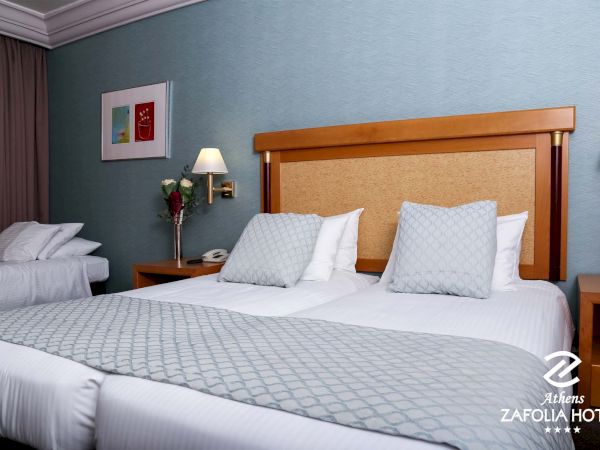 A hotel room with two beds, pillows, a headboard, nightstands, and lamps on a blue wall.