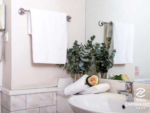 A bright hotel bathroom with white towels, eucalyptus flowers, a wall phone, a sink and chrome faucet.