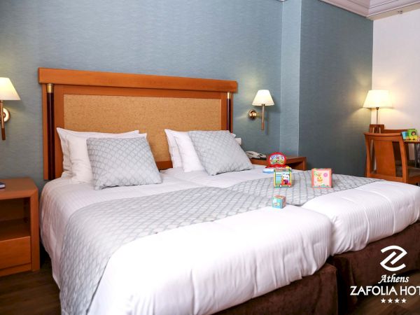 A hotel bedroom with a neatly made bed, pillows, bedside lamps, and children&rsquo;s toys on the nightstands.