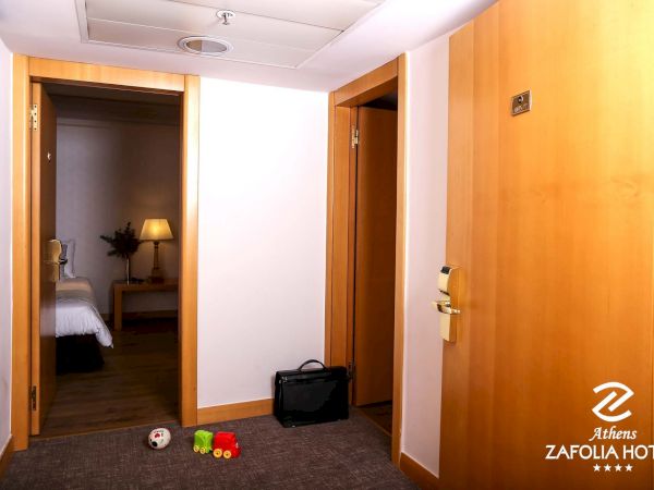 Hotel room entry hall with wooden doors, a closed suitcase, and toys on the carpet beside the bathroom.