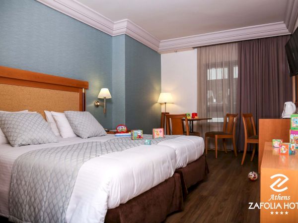 A hotel room with two beds, bedside lamps, curtains, a TV on the wall, and kids&rsquo; toys on the floor and table.