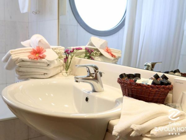A hotel bathroom scene with a white sink, chrome faucet, folded towels, toiletries in a basket, and flowers on the counter.