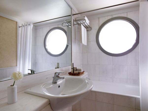 A modern bathroom sink with a faucet, towel hooks, and two bright round mirrors over white tile walls.