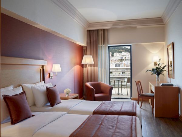 A modern hotel room with twin beds, lamps, and a balcony view through tall windows.