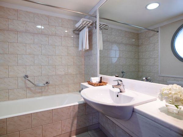 A bright bathroom with a bathtub, sink, towel rail, and shower fixtures against marble tiles.