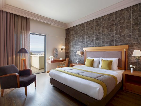 Modern hotel bedroom with a king bed, bedside lamps, green accents, curtains, and a balcony door with view.