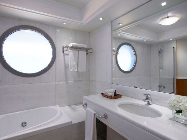 Modern bathroom featuring a bathtub, double sink vanity, round backlit mirrors, towel racks, and a glass shower enclosure.