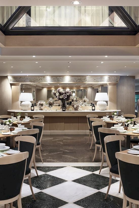 An elegant dining hall with neatly set tables, floral centerpieces, and warm ceiling lights arranged for a formal banquet.
