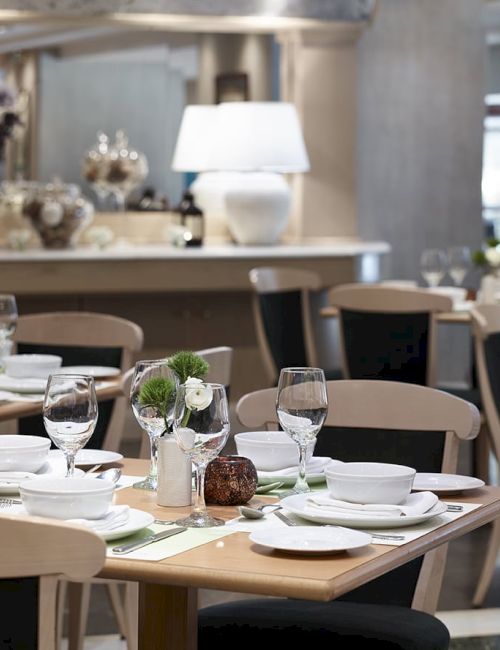 An elegant restaurant dining area with neatly set tables&mdash;plates, wine glasses, flowers, and a warm lamp lighting the scene.