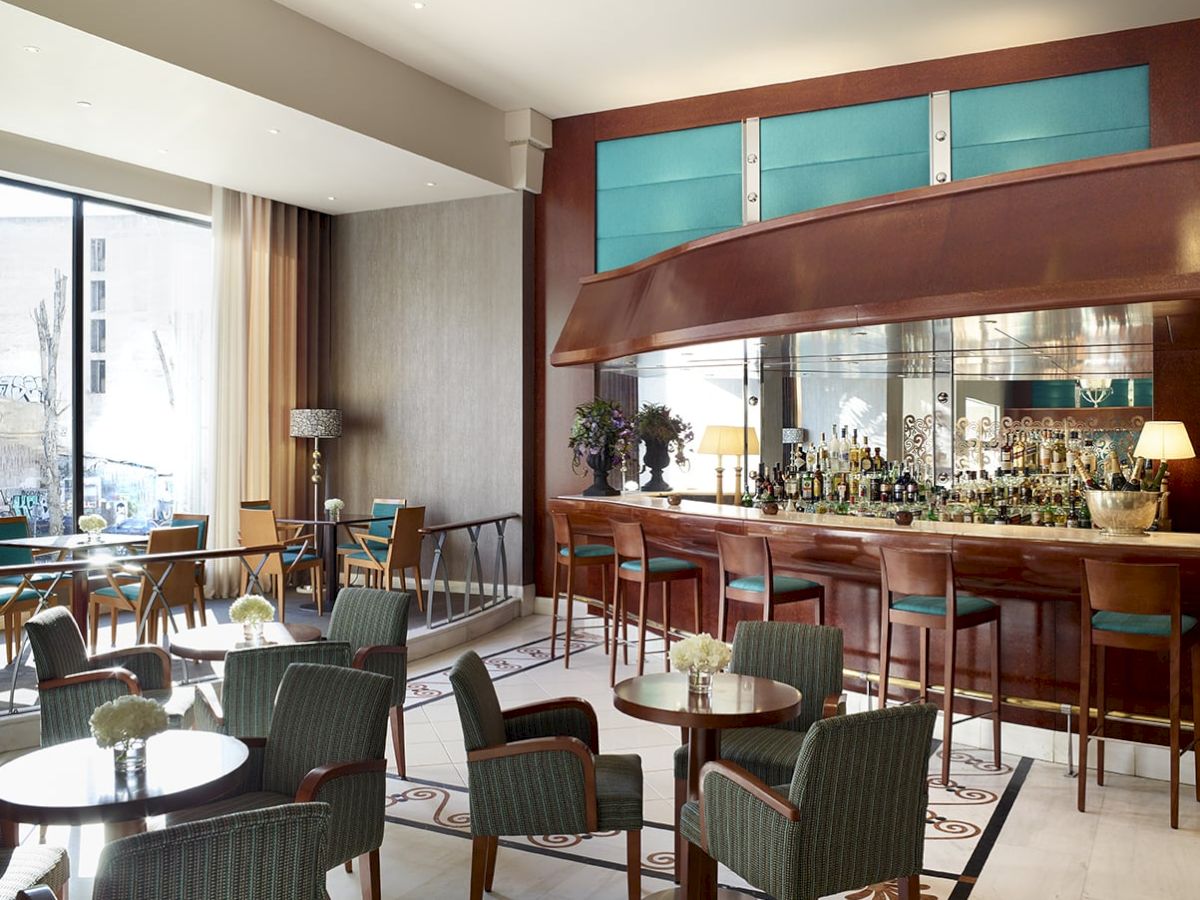 Modern hotel bar lounge with chairs, tables, and a wooden back bar stocked with bottles.