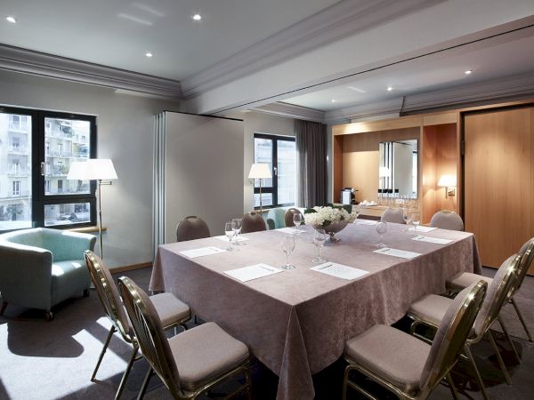 A modern meeting room with a set dining table, chairs, soft lighting, and windows overlooking a city.