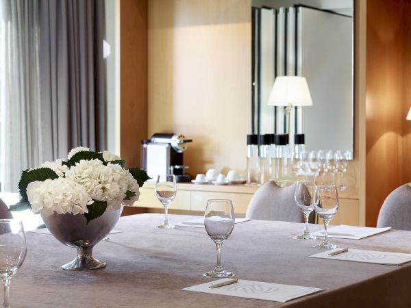 A formal hotel dining room table set with white flowers, wine glasses, and place cards under warm lamps.