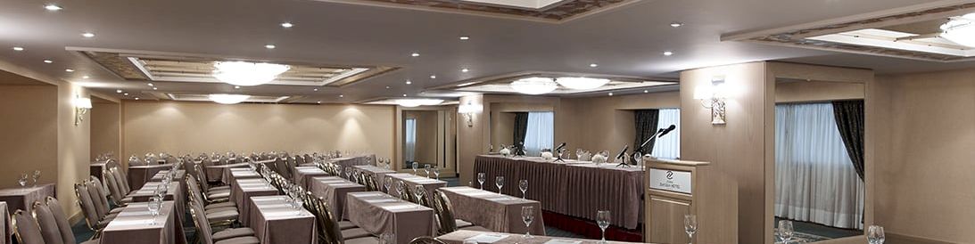 A banquet-style conference hall with long tables set with linens, glasses, place cards, and microphones for speeches.
