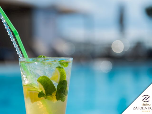 A minty green drink in a glass with a striped straw, served by a blue pool.