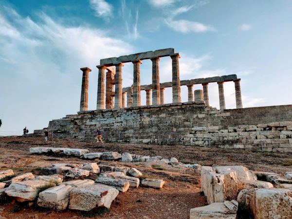 Ancient temple ruins with tall stone columns on a rocky site under a dramatic blue, cloud-filled sky.