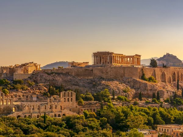 Sunset over Athens&rsquo; Acropolis, with the Parthenon&rsquo;s towering columns and the surrounding ancient ruins on the hilltop.