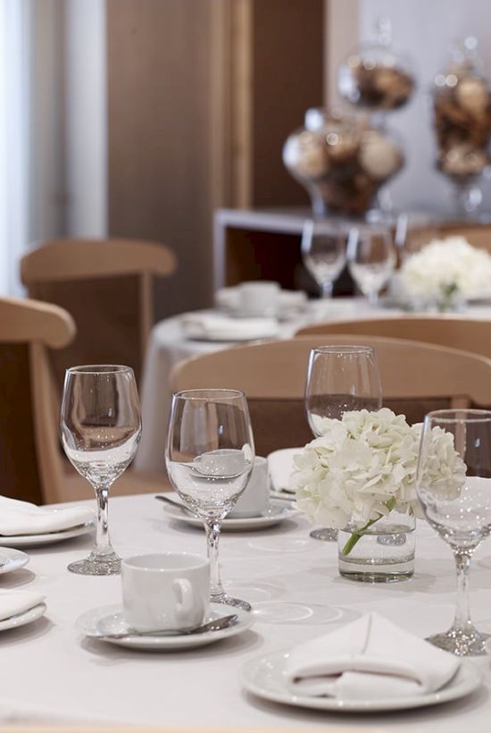 A formal banquet table set with white flowers, crystal wine glasses, cups, plates, and two decorative centerpieces.