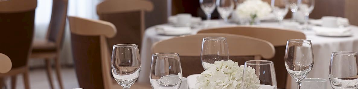 A beautifully set dining table with wine glasses, teacups, white flowers, and candles in a warm indoor setting.