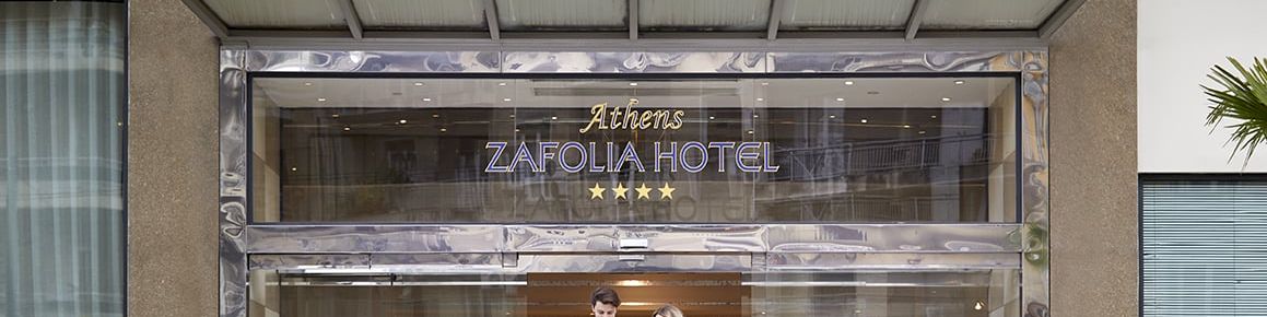 Entrance of Athens Zafolia Hotel with glass doors and two guests walking inside.