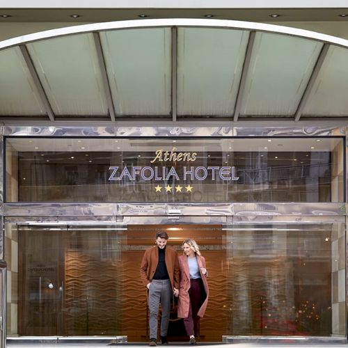An exterior entrance to Zafolia Hotel, with two people walking in through a glass canopy.