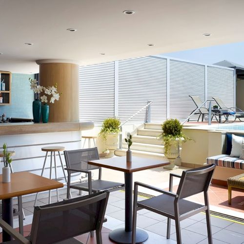 A stylish rooftop terrace with bar shelves, lounge seating, and a swimming pool behind privacy shutters.
