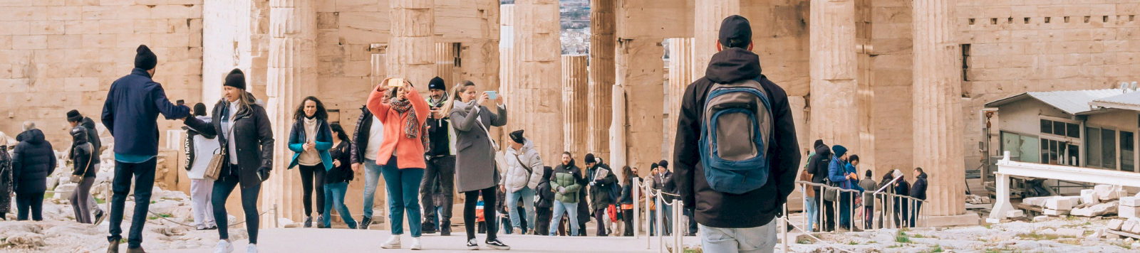 Tourists walk in front of the Parthenon at the Acropolis in Athens, Greece under a cloudy sky.