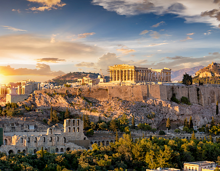 Athens’ Acropolis shines at sunset, with the Parthenon and surrounding ancient columns glowing in the golden sky.